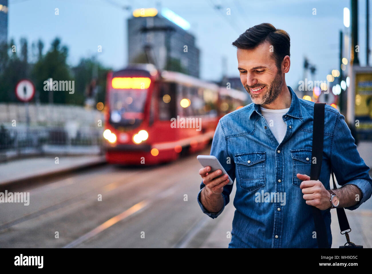 Man using smartphone while waiting for public tram in the evening Stock Photo