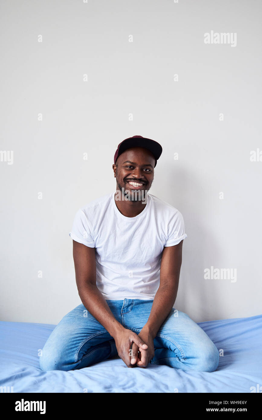 Portrait of artist sitting on bed looking at camera wearing cap Stock Photo