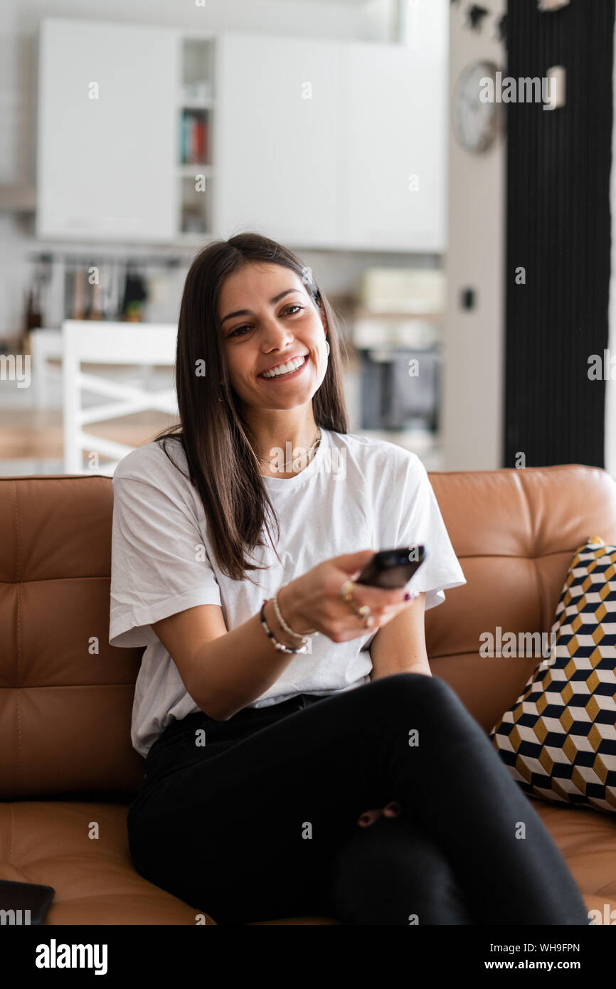 Happy young woman sitting on couch at home watching Tv Stock Photo - Alamy