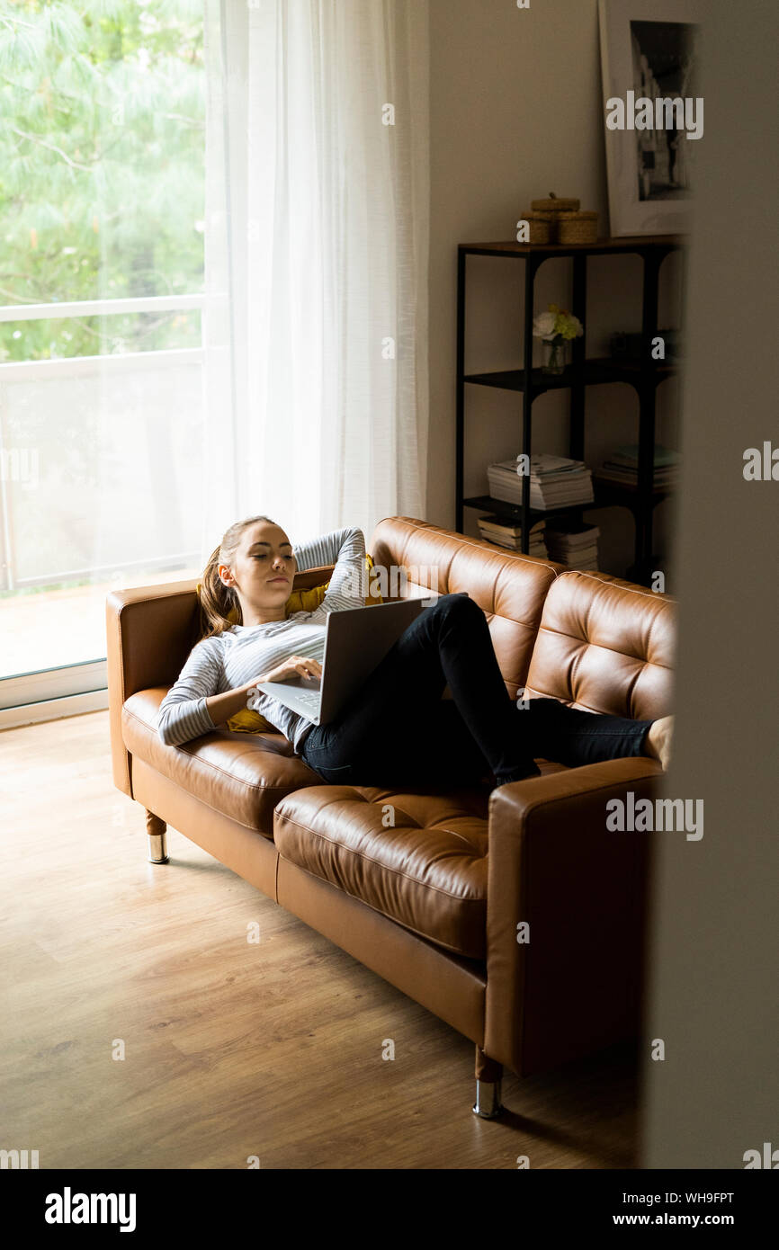 Young woman lying on couch at home using laptop Stock Photo - Alamy