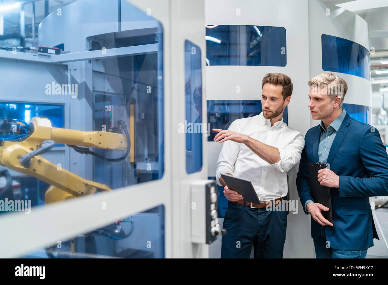 Two businessmen talking at robot in a modern factory Stock Photo - Alamy