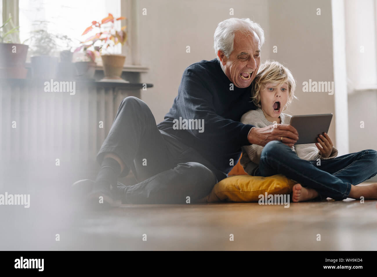 Screaming grandfather and grandson sitting on the floor at home using a tablet Stock Photo