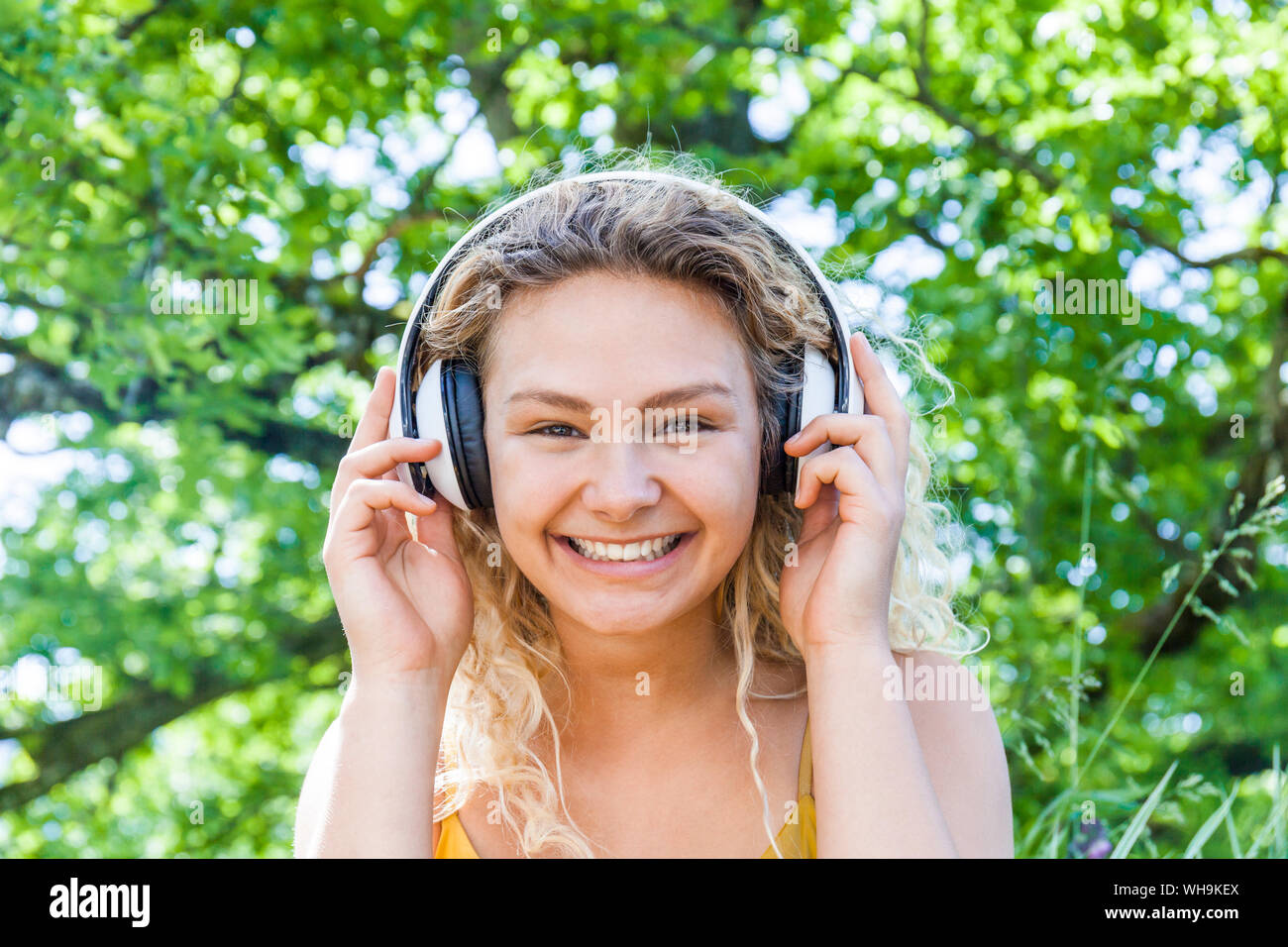 Smiling young woman listening to music, looking at camera Stock Photo