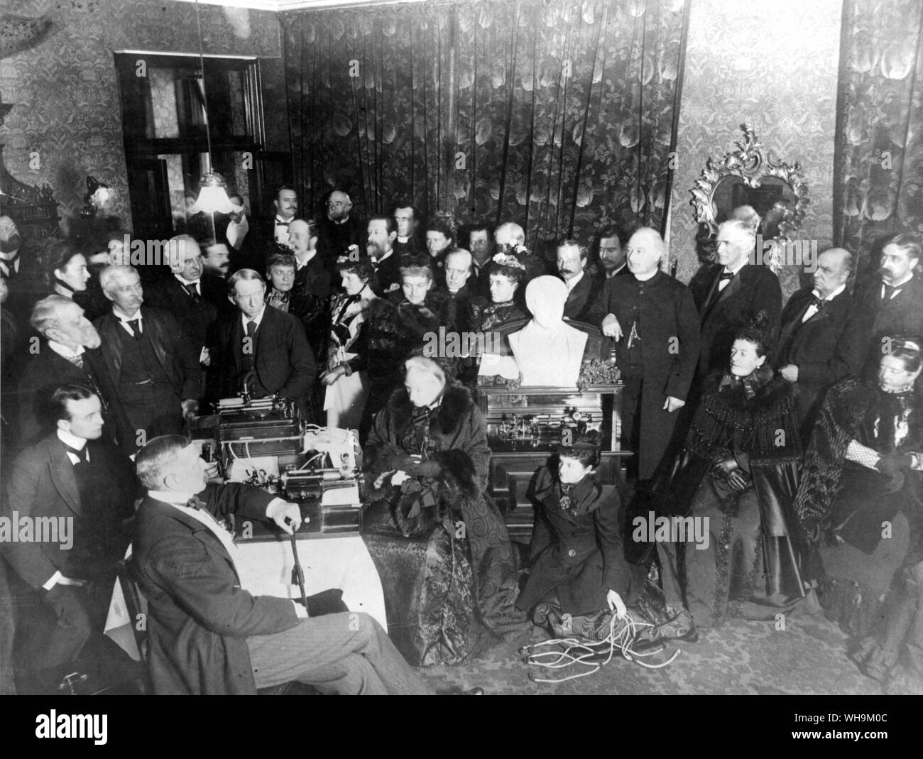 'A distinguished gathering in the early 1890s at Colonel Gouraud's flat in Whitehall, listeing to the phonographic record of Cardinal Newman's voice brought over from America by Colonel Goraud. Seated near the instrument is Lady Herbert of Lee and immediately behind her is Lady Jeune (Lady St. Helier). On the extreme right is the Duchess of Teck, and other distinguished people in the assembly are Lord Aberdeen, Sir H. M. Stanley, Sir Ellis Ashmead Bartlett, Sir Charles Russell (Lord Russell of Killowen) and Cardinal Vaughan. The bust in the centre is that of Thomas Edison. Stock Photo