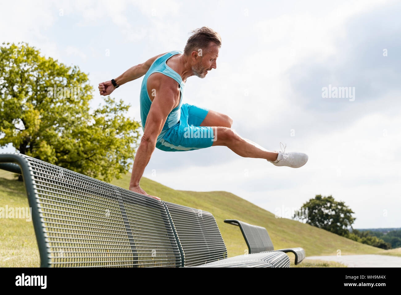 Sporty man jumping over a bench in a park Stock Photo