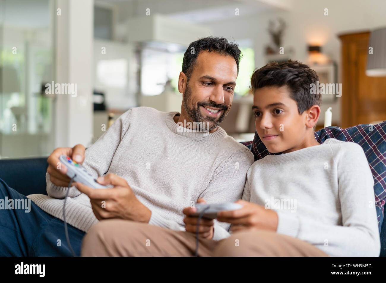 Happy father and son playing video game on couch in living room Stock Photo