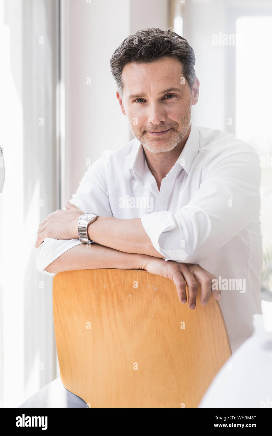 Mature man sitting on chair backwards, smiling Stock Photo Alamy