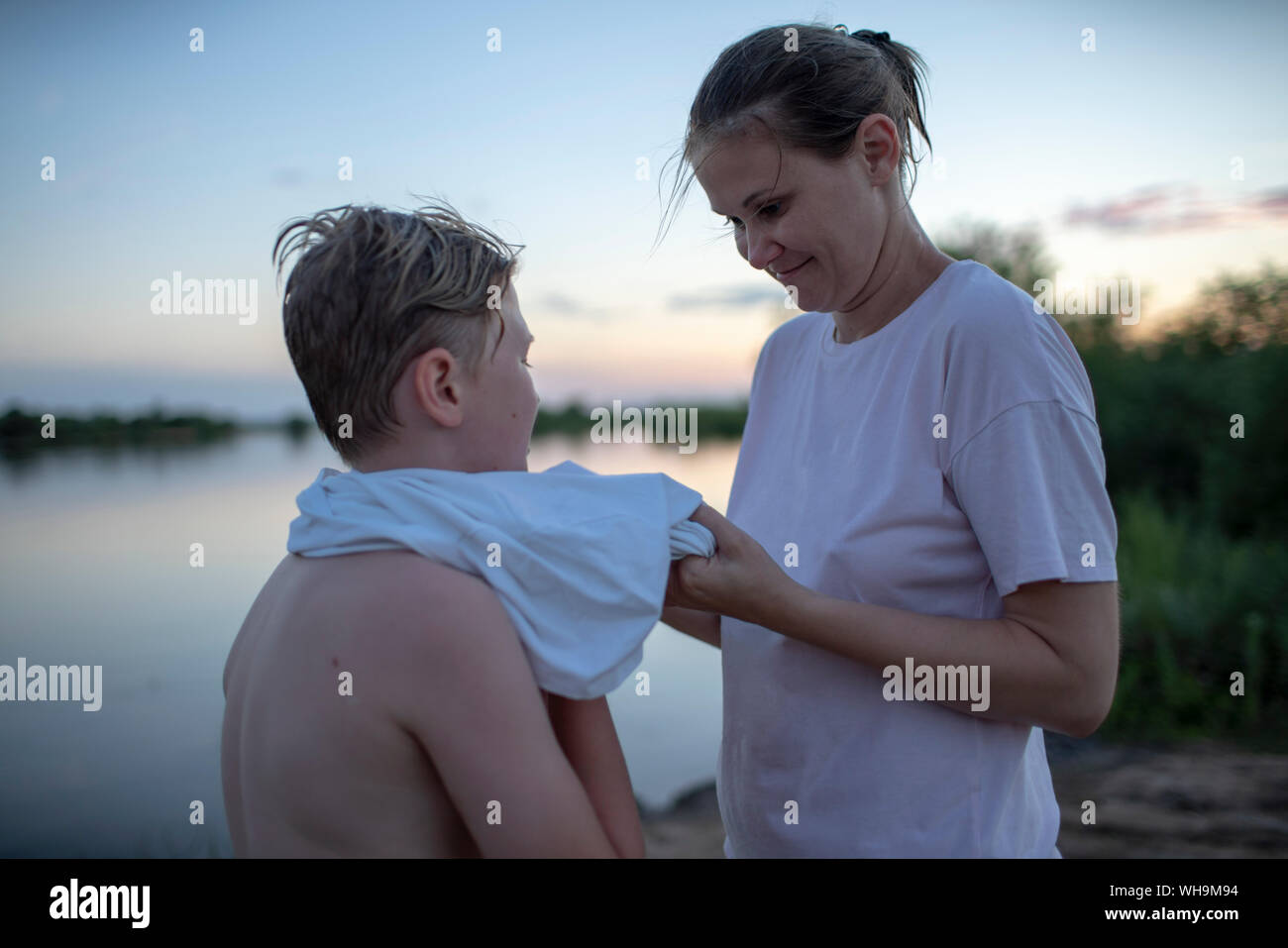 Mother caring for son at a lakeshore at sunset Stock Photo