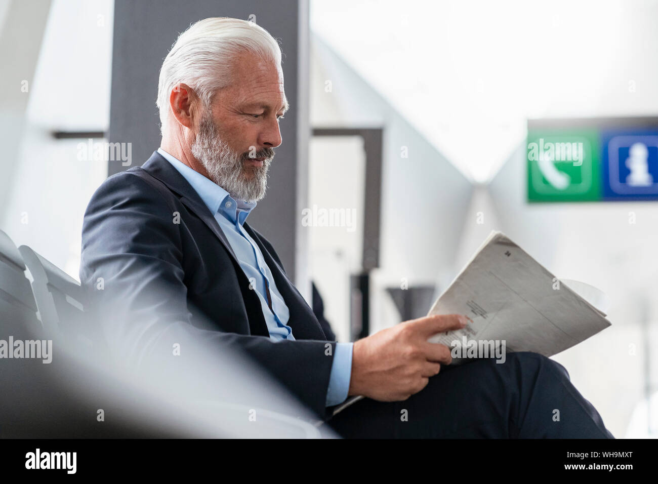 Mature businessman sitting in waiting area reading newspaper Stock Photo