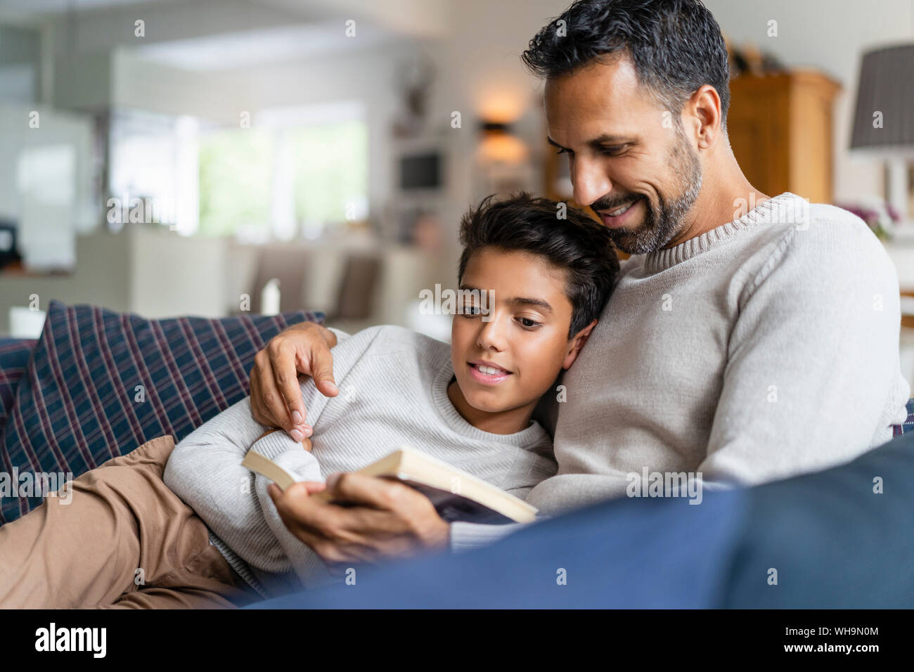 Father lying with son on couch in living room reading book Stock Photo