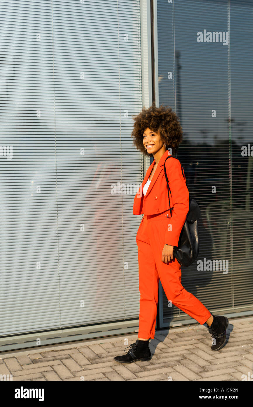 Smiling young woman with shoulder bag wearing fashionable red pantsuit Stock Photo