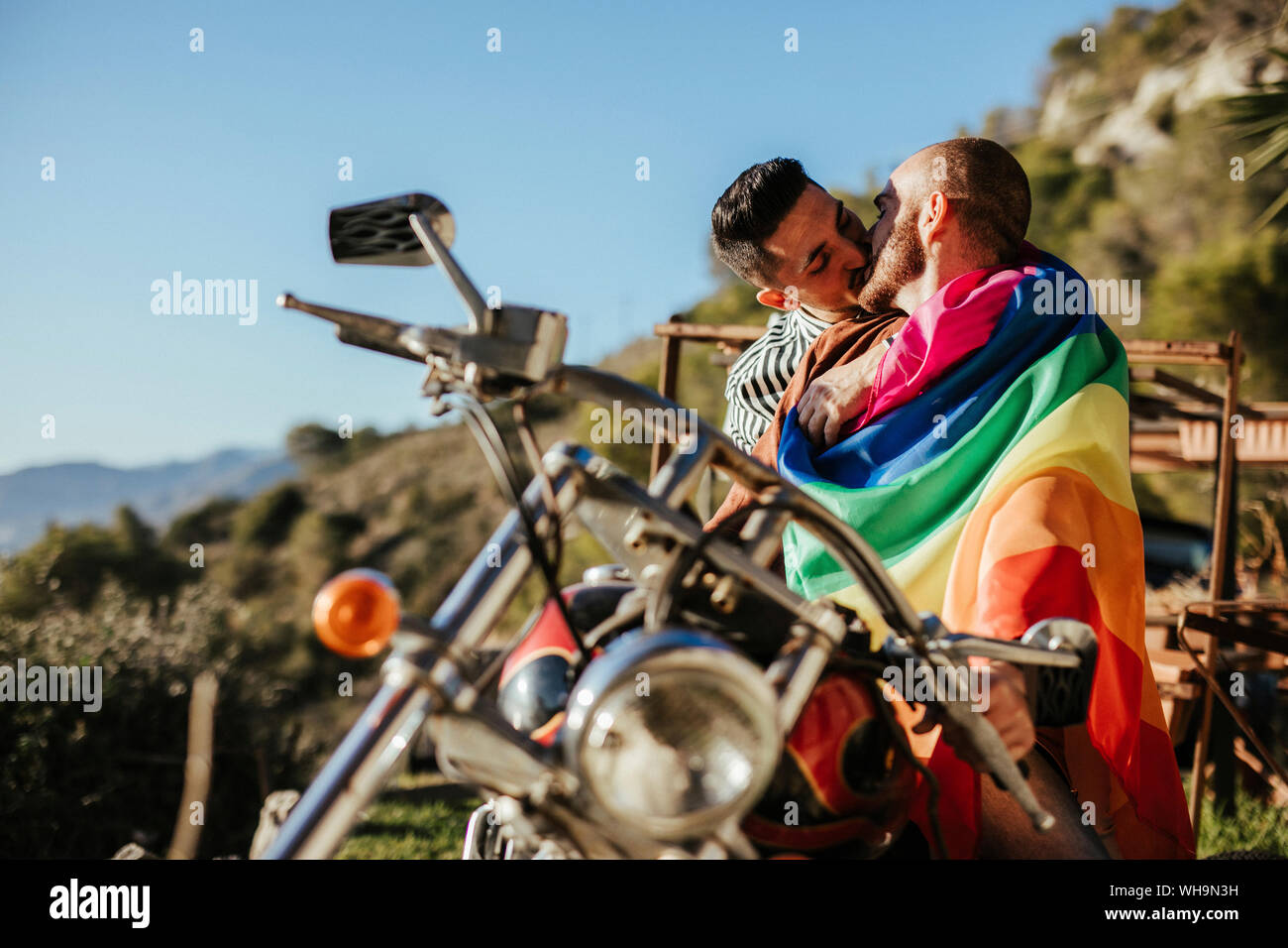 gay-couple-with-gay-pride-flag-kissing-on-a-motorbike-WH9N3H.jpg