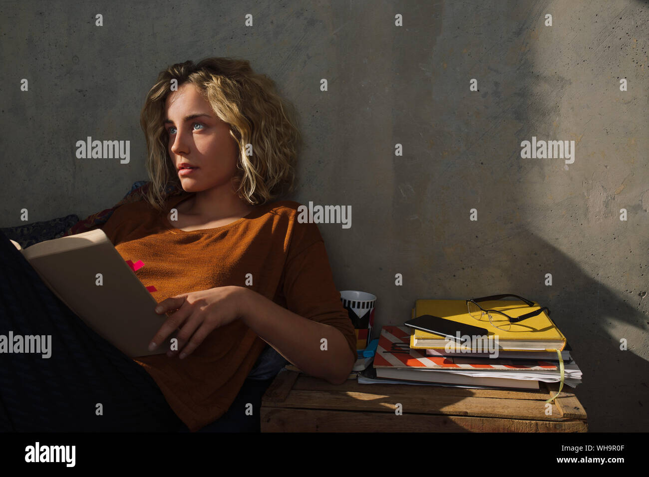 Pensive student sitting on bed with a book Stock Photo