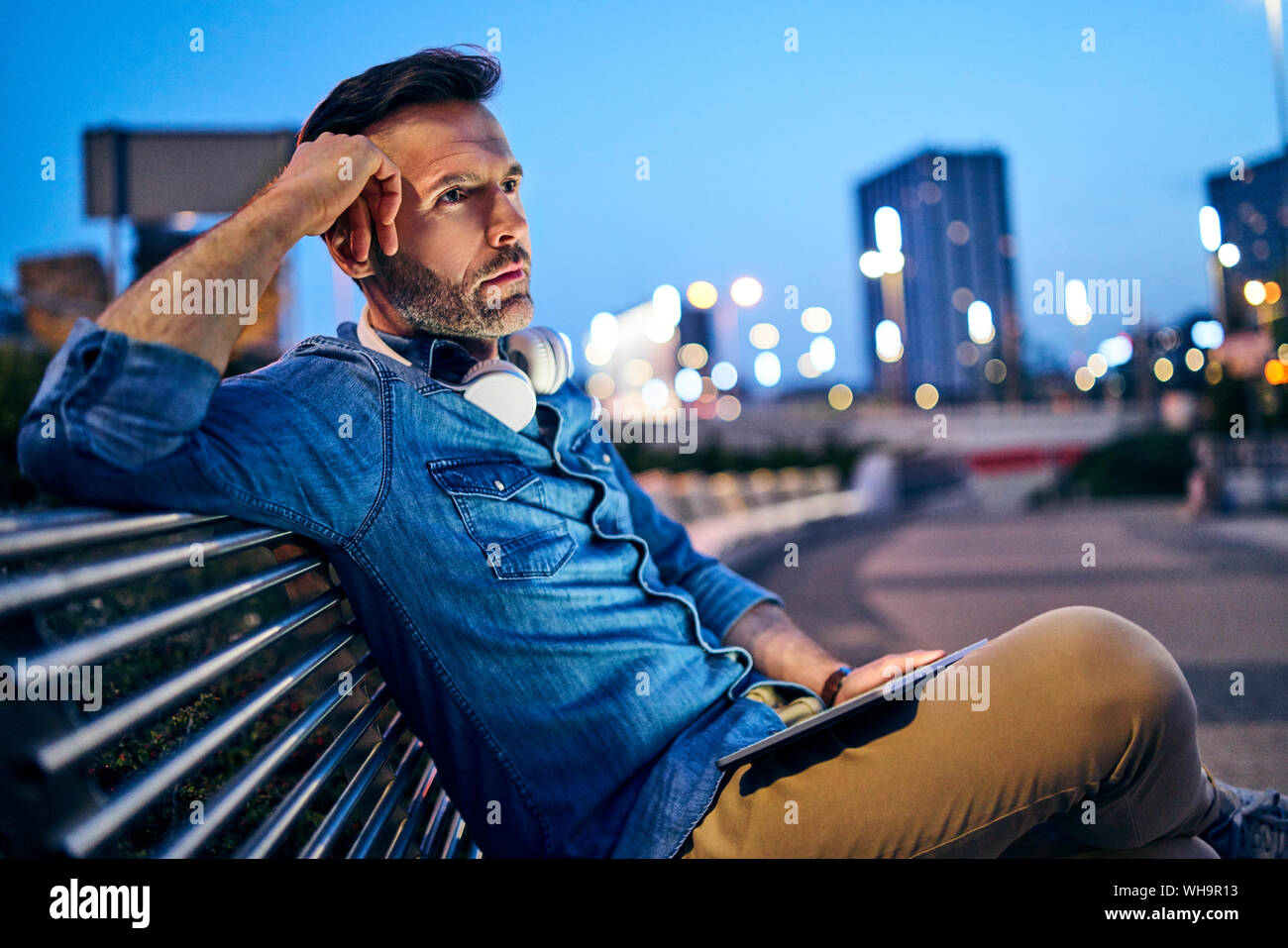 Worried man looking away while sitting on public bench with tablet Stock Photo