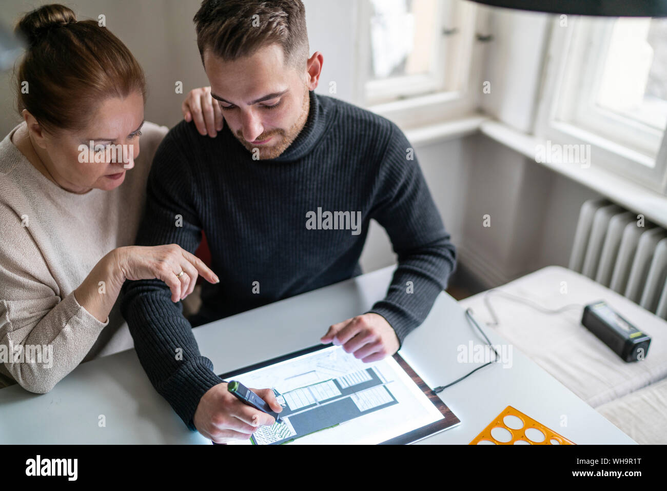Senior woman watching man using tablet with architectural plan Stock Photo