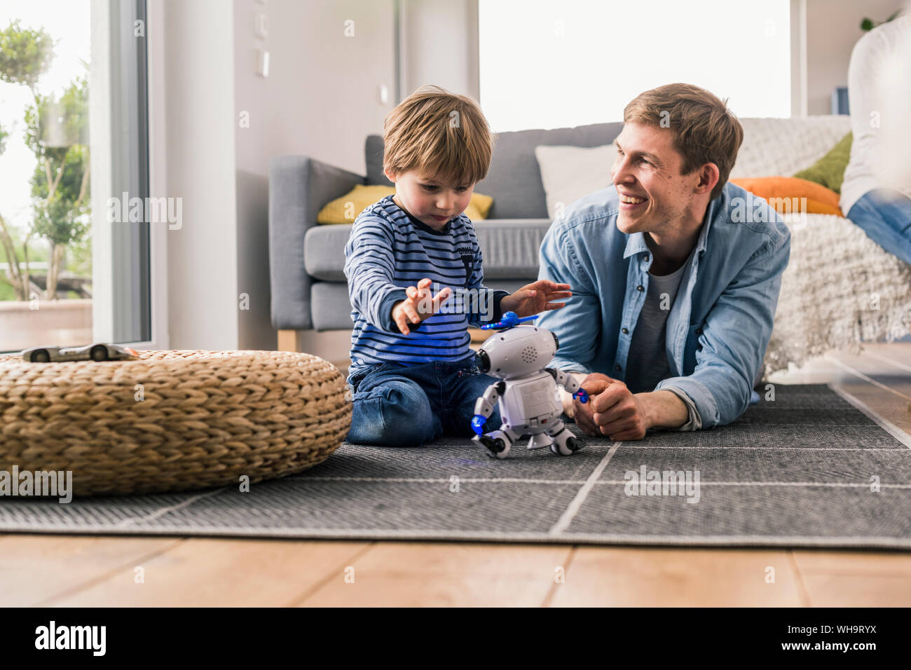Father and son lying on floor, playing with toy robot Stock Photo