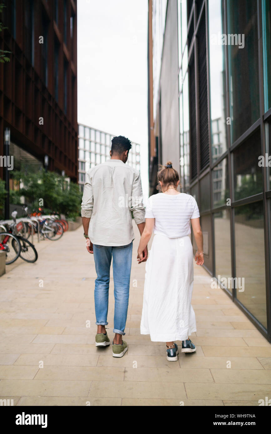 Back view of young couple walking hand in hand on pavement Stock Photo ...