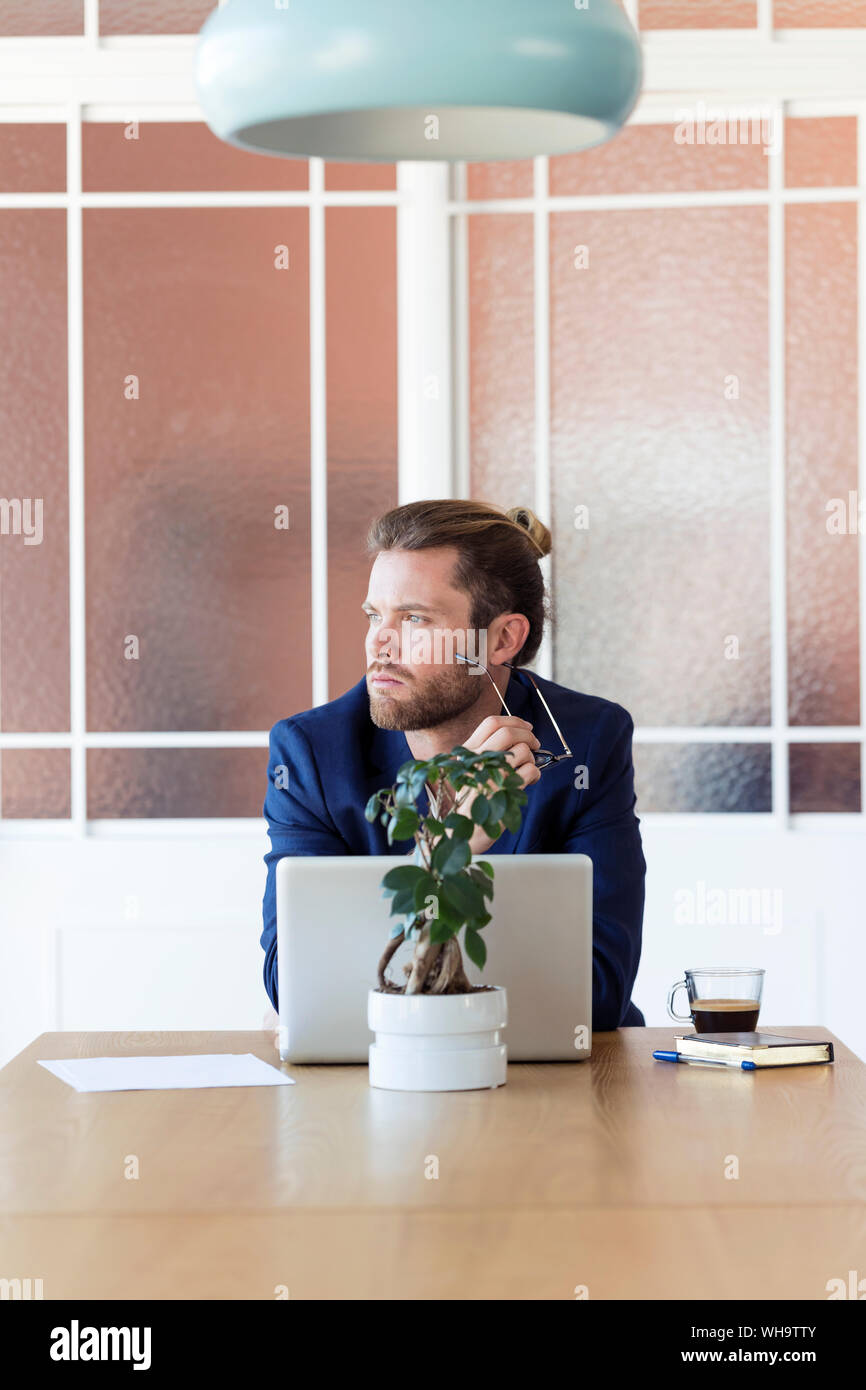 Pensive businessman with laptop at table in office Stock Photo