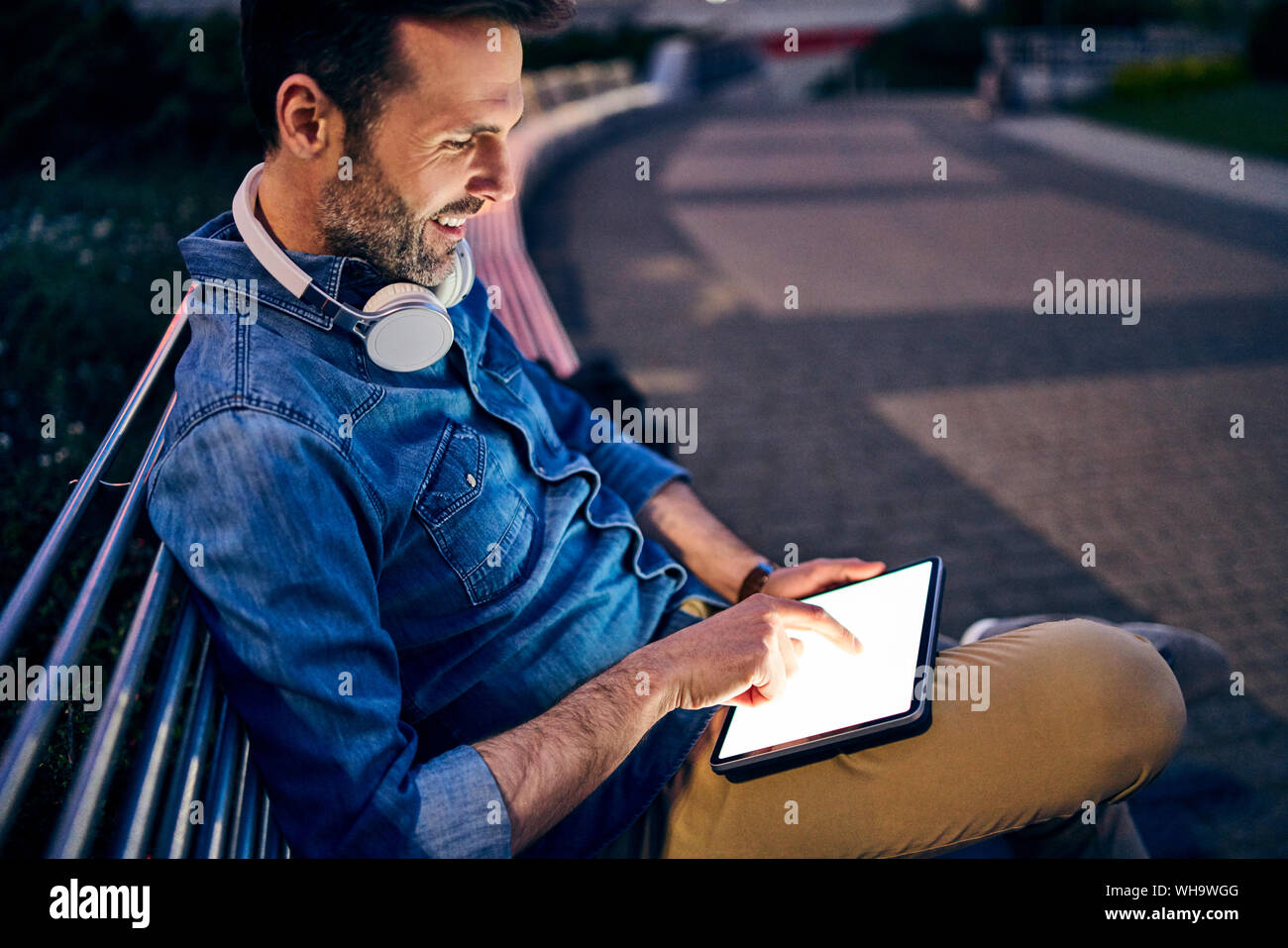 Man using tablet while sitting on a bench in the city in the evening Stock Photo