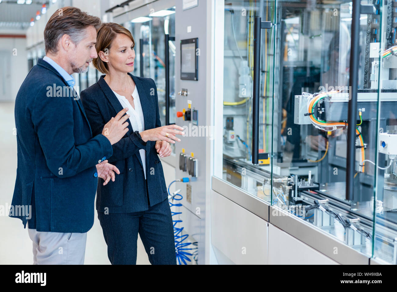 Businessman and businesswoman looking at a machine in a modern factory hall Stock Photo