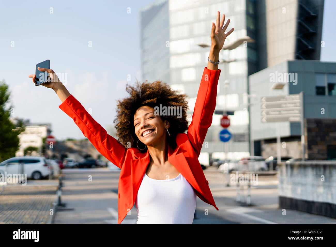 Portrait of happy young woman with smartphone wearing fashionable red suit jacket Stock Photo
