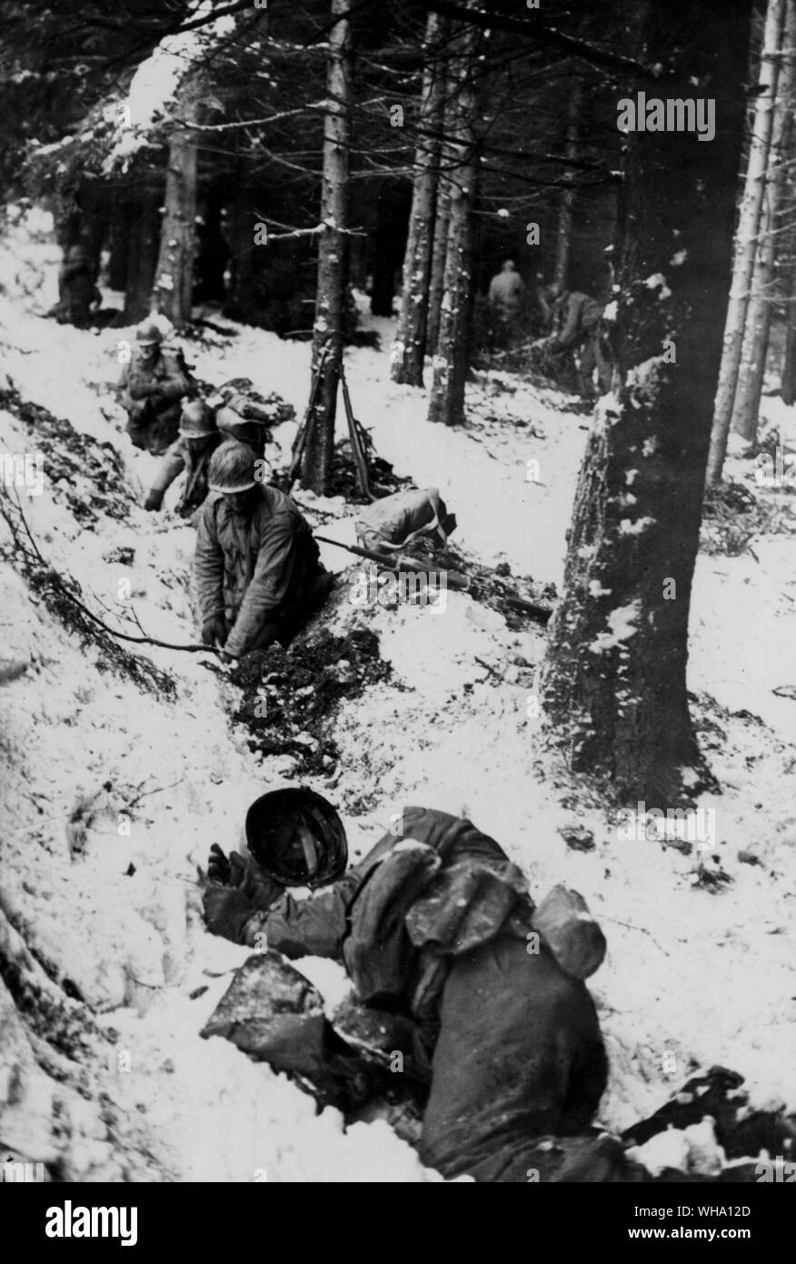 WW2: American soldiers dig hasty foxholes in snow-covered terrain as enemy artillery fire opens up near Berismenil, Belgium. Soldier lying in foreground has been stricken down. Ardennes campaign, Dec. 1944. Stock Photo