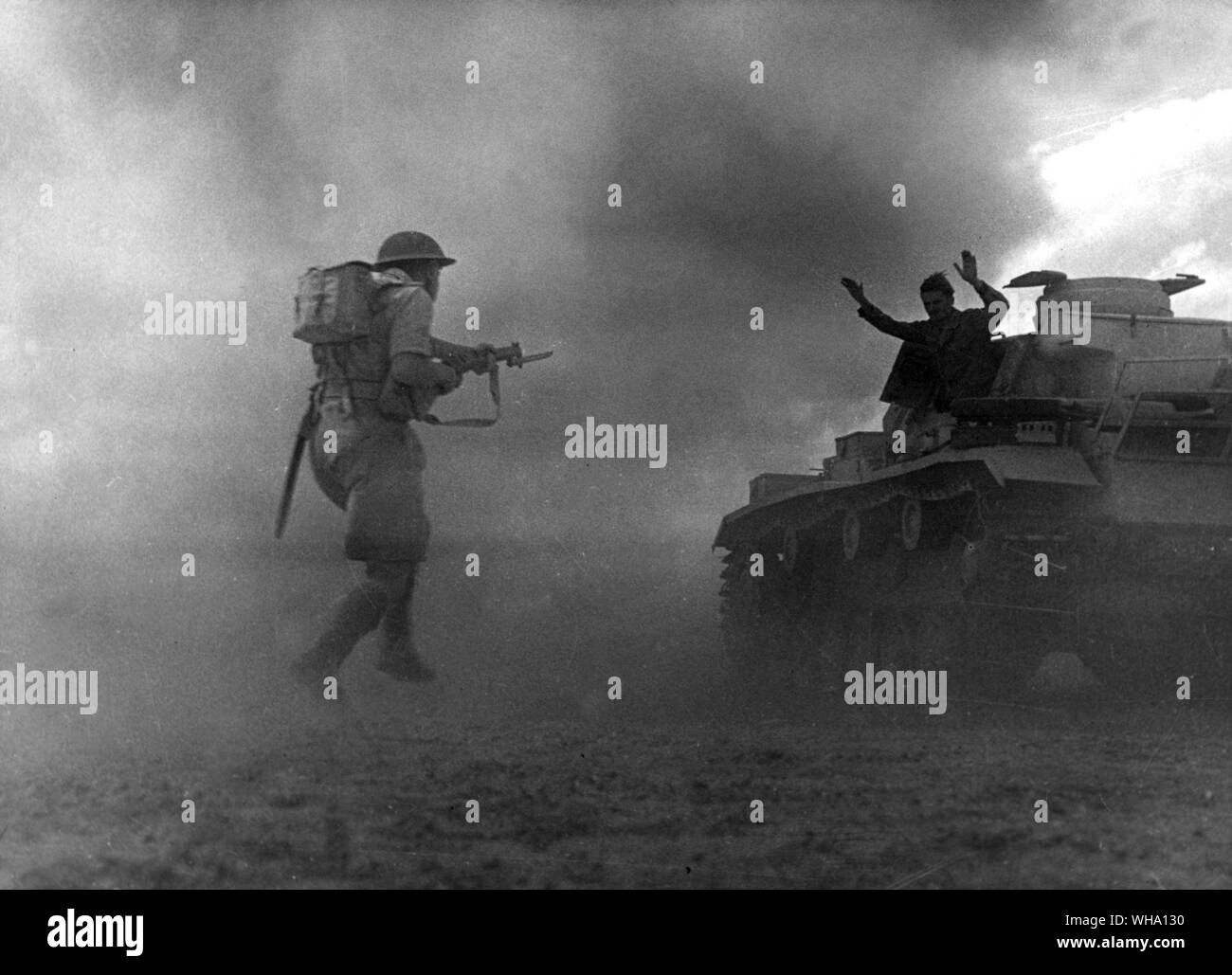WW2: One member of a knocked out German tank surrenders as British Infantry rush his tank at Alamein. 1942. Stock Photo