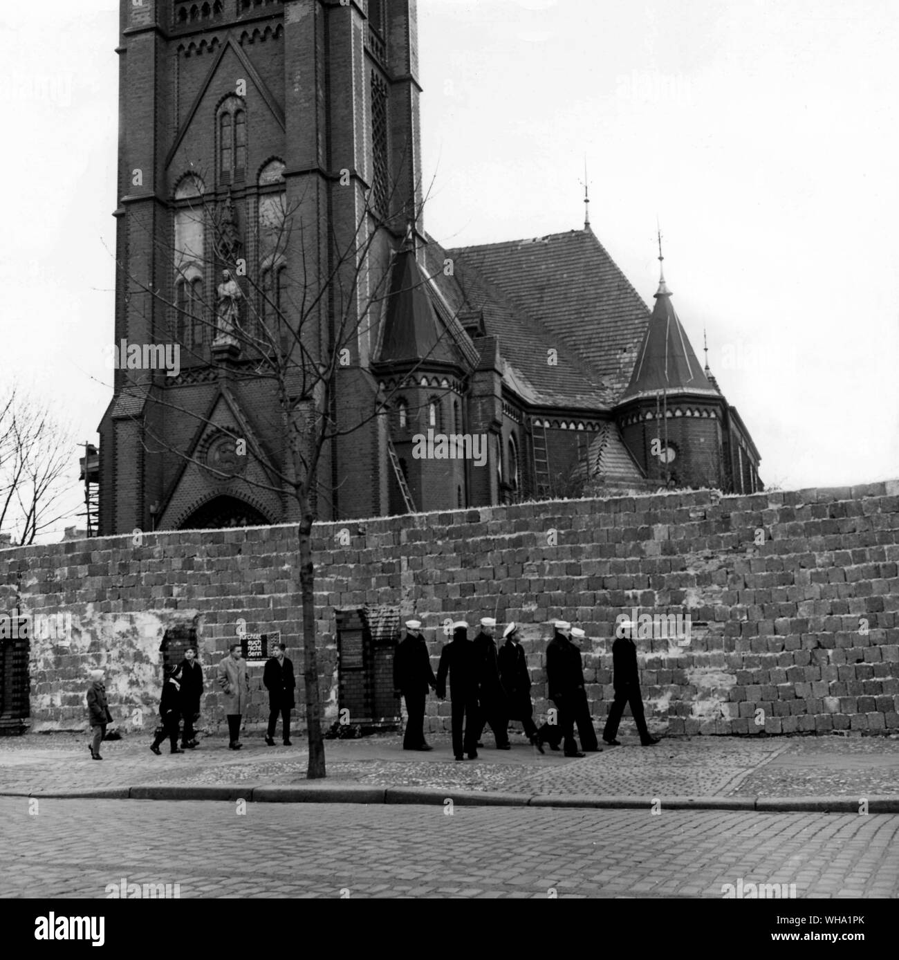 US Navy reserves touring Berlin are a strange sight to the people in the divided city, so German children find easy reason to follow the sailors as they walk next to the brick dividing wall. US navy photo. (is this WW2 or post WW2?) Stock Photo