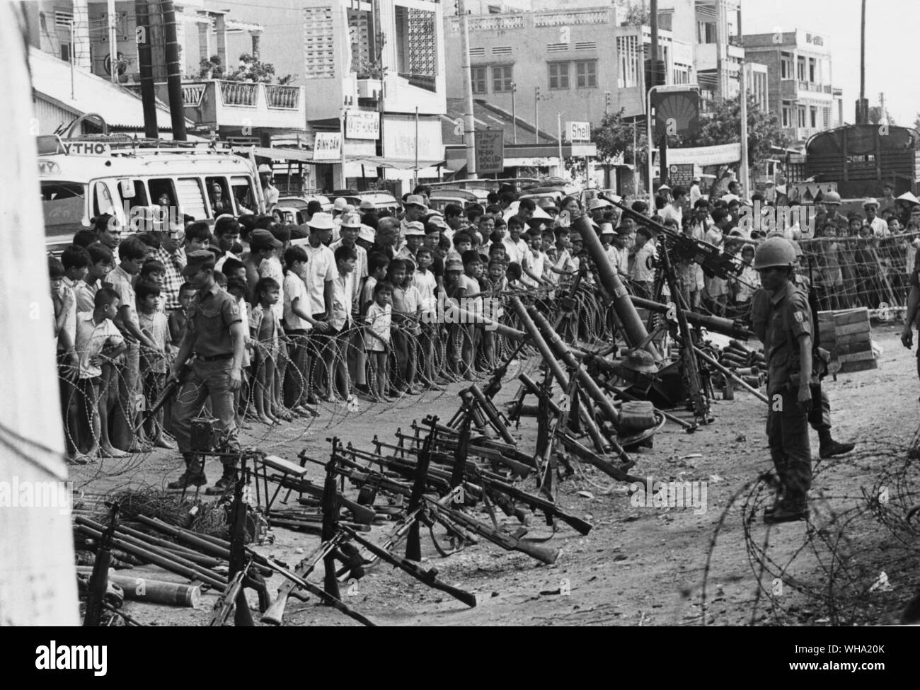 Vietnam war: Vietnaese soldiers behind a barbed wire barricade with civilians looking on. Stock Photo