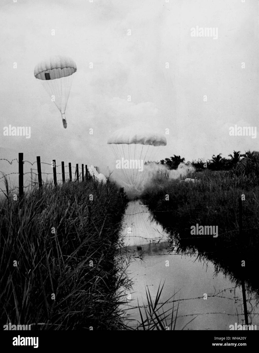 Vietnam war: A rice drop in South Vietnam. A parachute and its load of rice drops squarely into the protective moat surrounding the village of Luong Hoa. Another is on its way down. Stock Photo