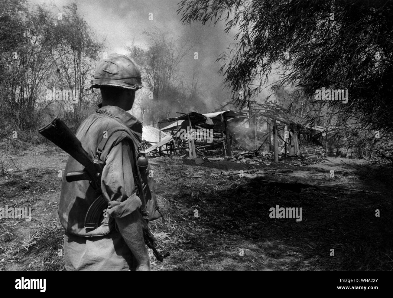 Vietnam war: An American soldier in front of the burning remains of one of the houses in Phu Lam. After the fires died down, he and one of his comrades were to go through the village to make sure no Viet Cong fighters were concealed in tunnels under the houses. 1968 Stock Photo
