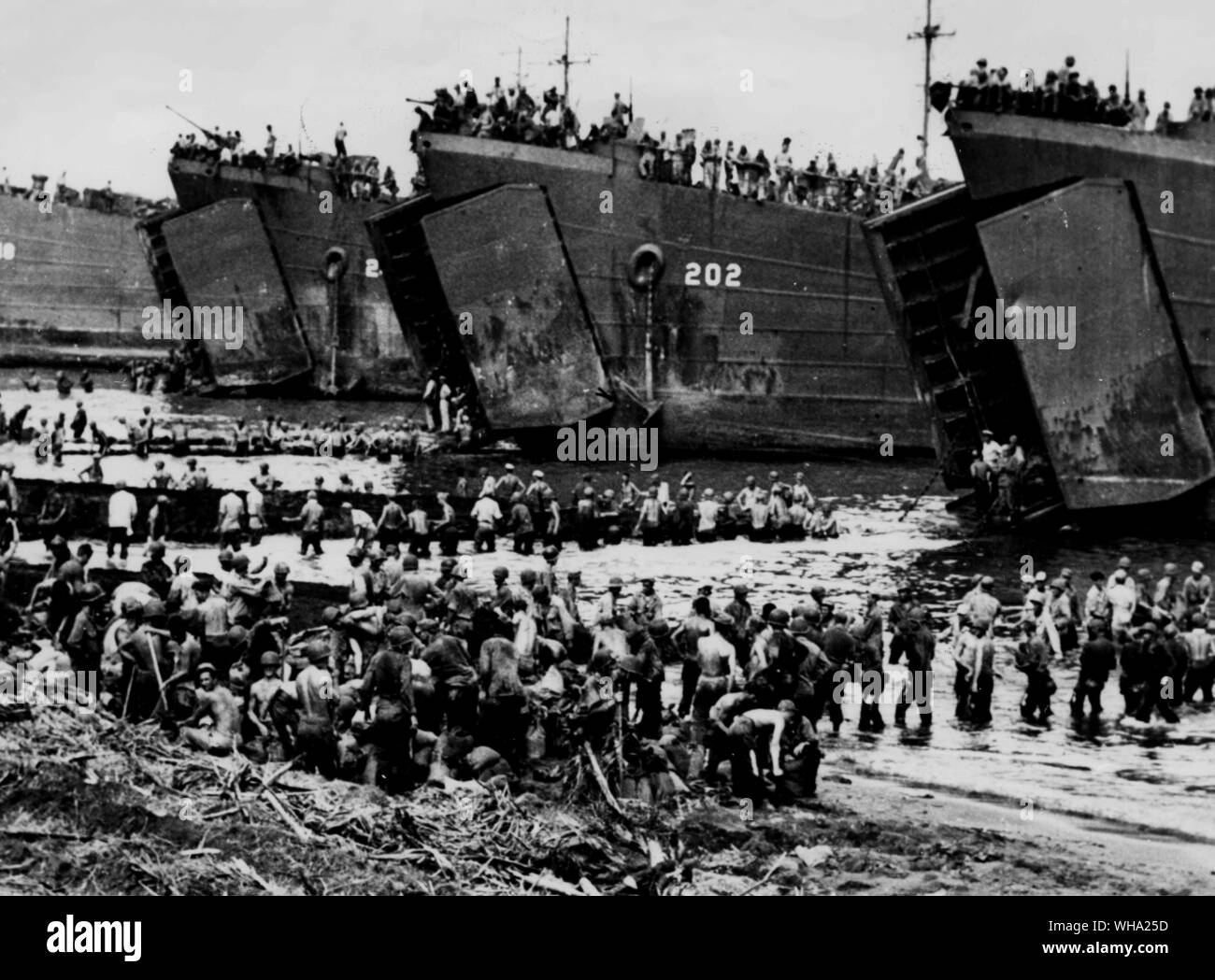 WW2: Knee deep in water off the beach at Leyte Island, American troops build temporary decks out to the gaping jaws of the landing ships and tanks which stand by waiting to dispatch their cargoes of war material. Stock Photo