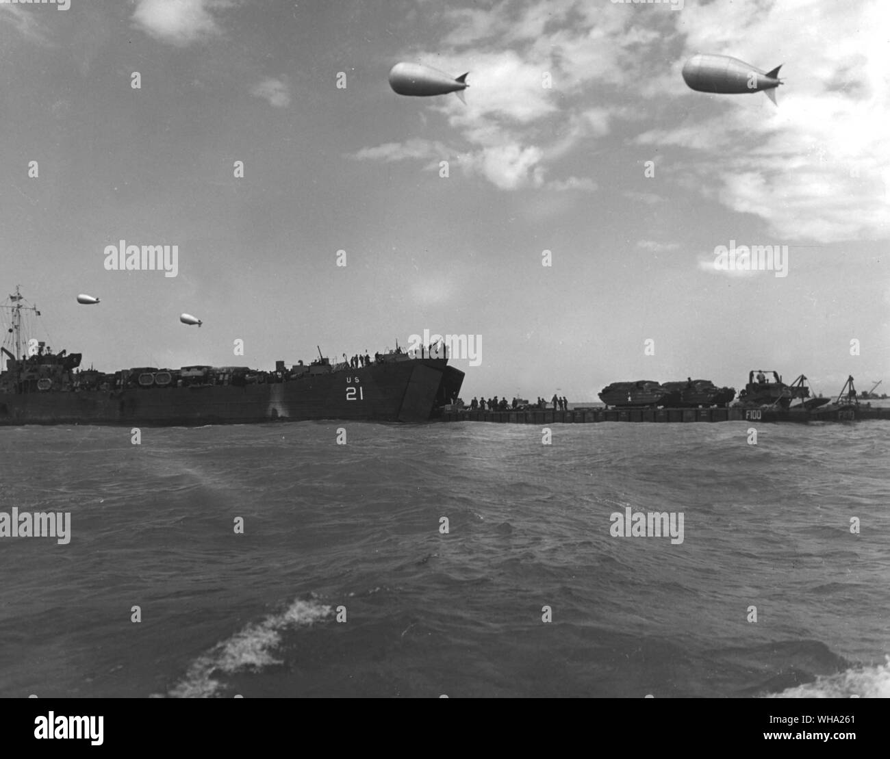 WW2: Protected from straffing Nazi planes by barrage balloons, a coast guard tank landing ship (left) forward passes a load of mechanised fighting vehicles to flat top of a rhino in the English in the English Channel during the height of the invasion of the French coast. The Rhinos slogged through the surf to unload their cargoes on the beach. Stock Photo