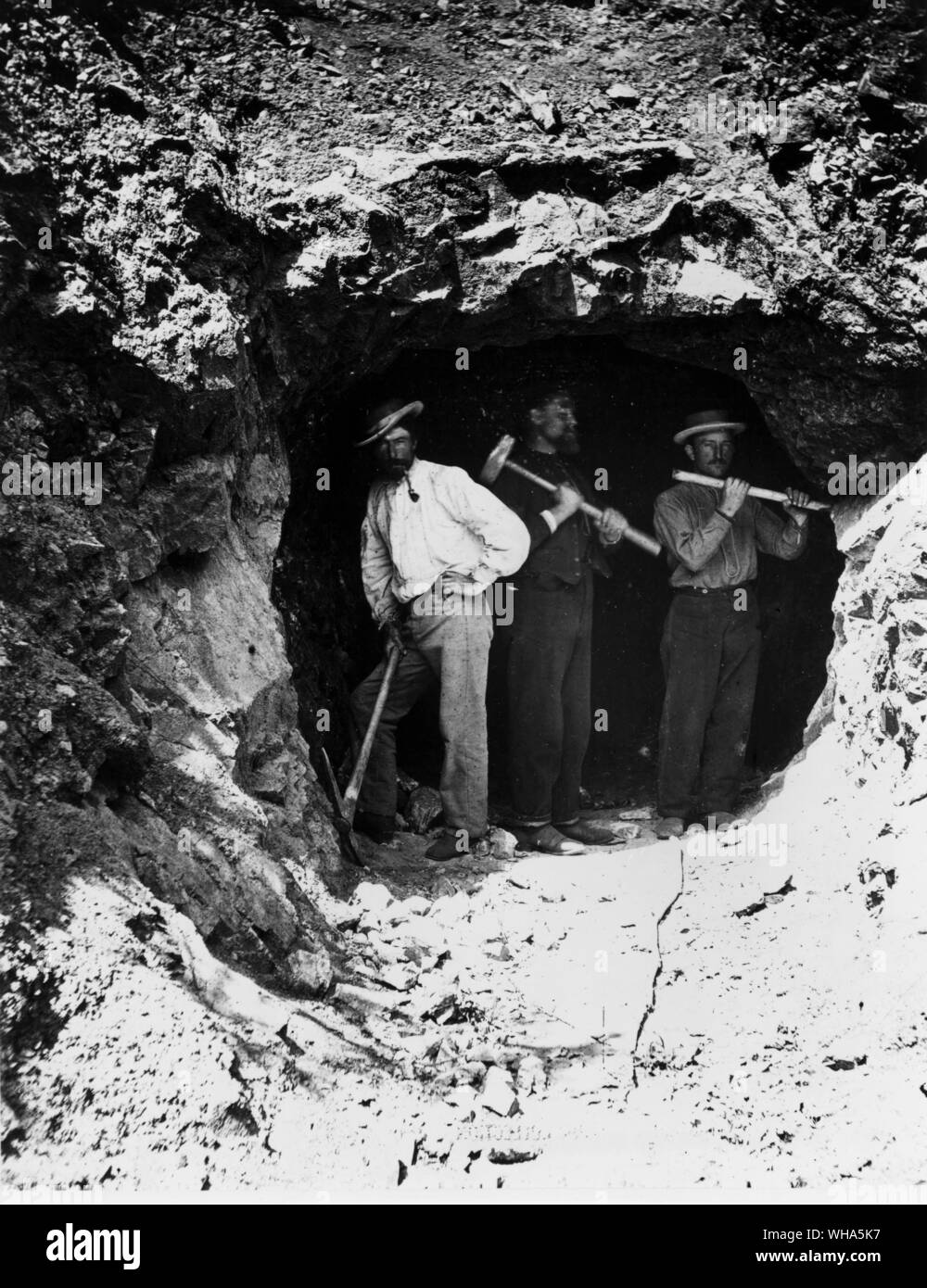 Three men standing in a tunnel, these men have just begun to bore one of three tunnels through the rugged Wasatch Mountains. The pair on the right are drilling a hole in which to set a charge of blasting powder. Photo by Russell 1868 Stock Photo