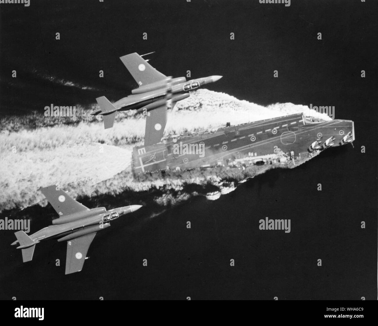 2 Buccaneer strike aircraft streak over HMS Eagle. To obtain this picture a Navy Aircraft rolled on its back 80 ft above the Buccaneers, a remarkable example of precision flying with 3 moving aircraft a moving ship and split second timing. October 1964 Stock Photo