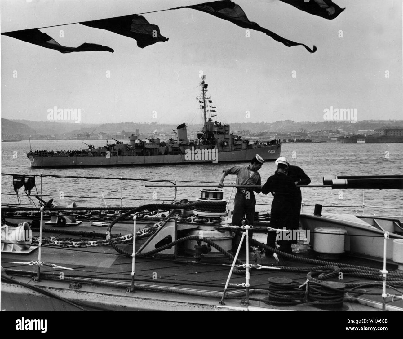 Dutch Frigate Dubois arrives at Cherbourg as men on British destroyers clean gun barrel, Ship armed in honour of Kings Birthday Stock Photo