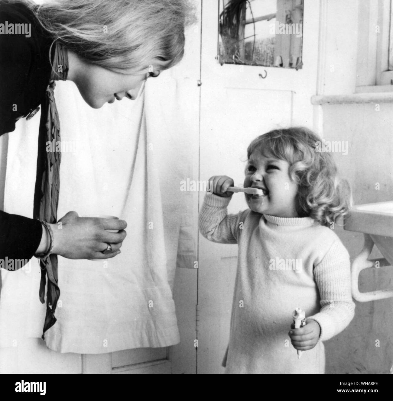 Woman watching over little girl brushing her teeth Stock Photo