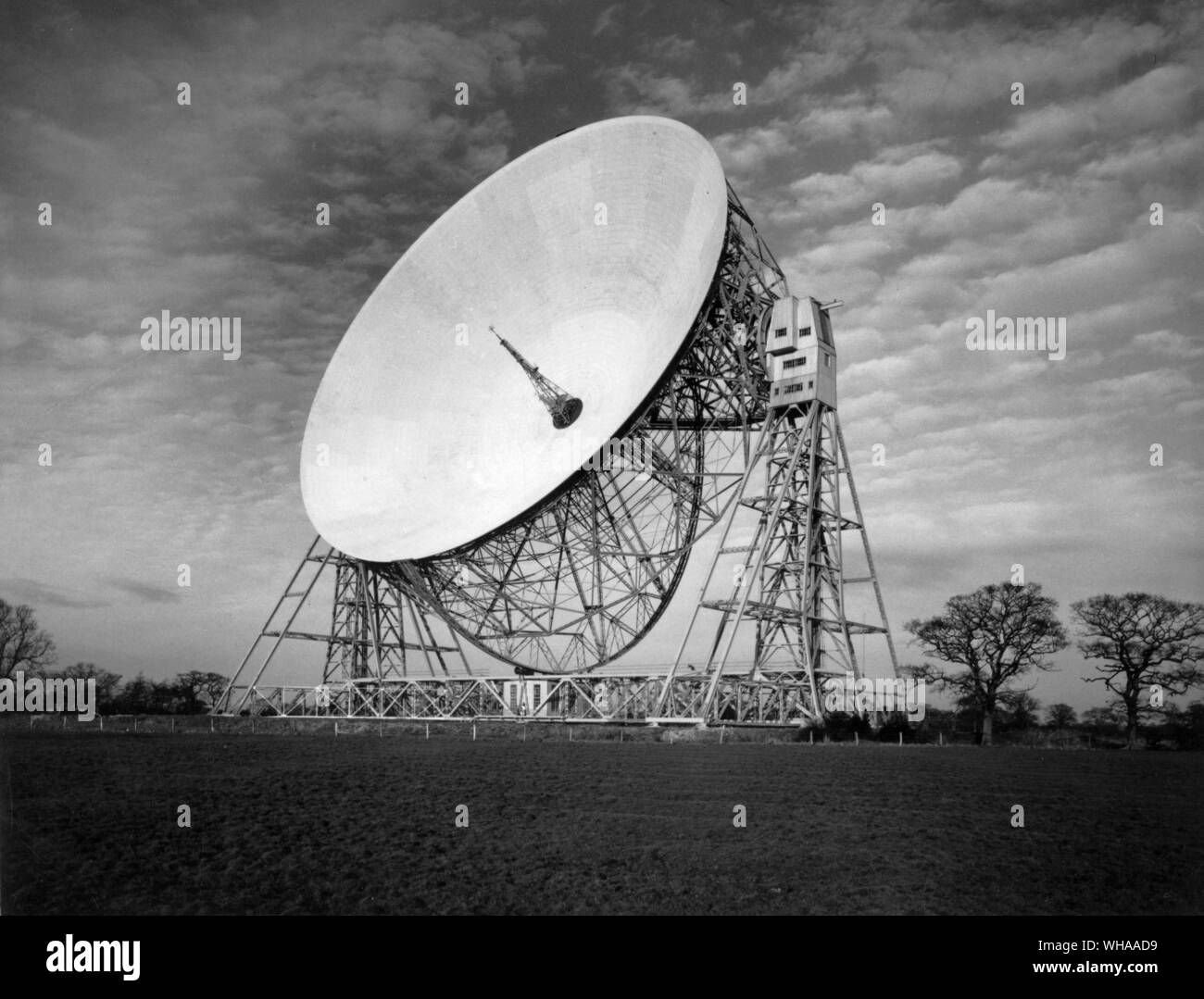 After nearly 10 years of planning the Jodrell Bank radio telescope the largest fully steerable one in the world was completed in time to take part in the International Geophysical Year of 1957-58. Powered by electric motors it can be driven to counteract the motion of the earth in order to follow automatically a planet star meteor or artificial satellite. It can penetrate deeper into space than any other form of telescope to ' hear ' radio signals emitted millions of light years ago. The bowl which can be rotated or tilted in any direction gathers and concentrates radio waves as an optional Stock Photo