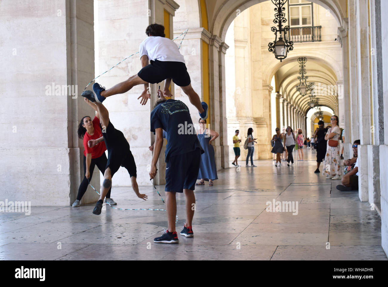 Four young people practising acrobatic double dutch with synchronised leap frogging and a cart wheel in Lisbon public walkways near Rua Augusta Arch Stock Photo