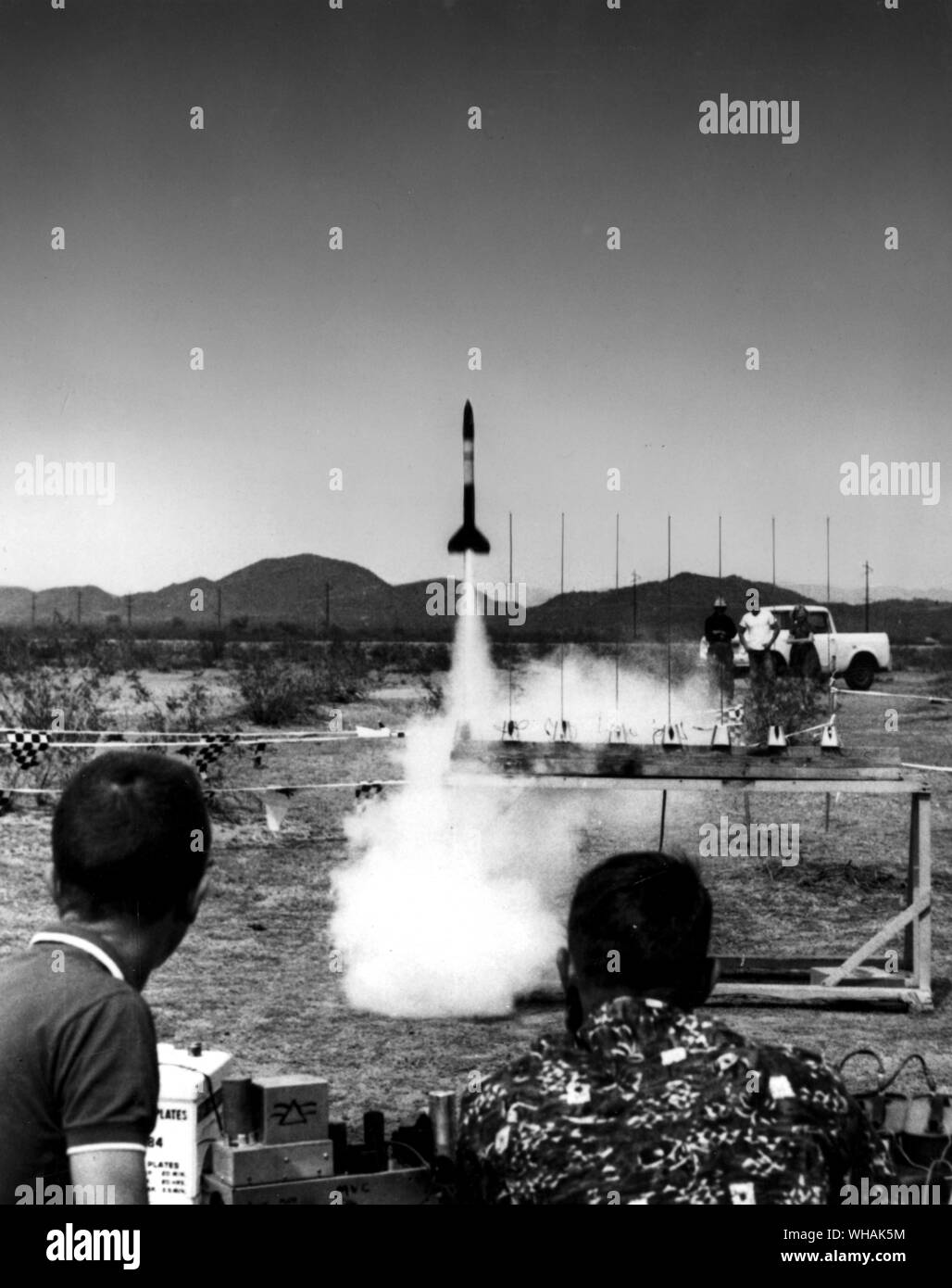 Safety First, observers keep a safe distance as a model rocket soars skywards Stock Photo