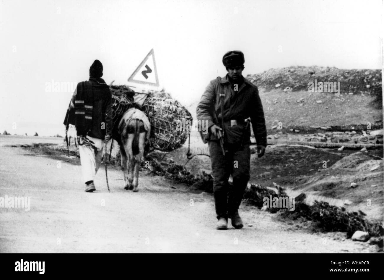 Kabul Afghanistan. Russian soldier on patrol passes Afghan villager and his donkey on lonely mountain road near Kabul Stock Photo
