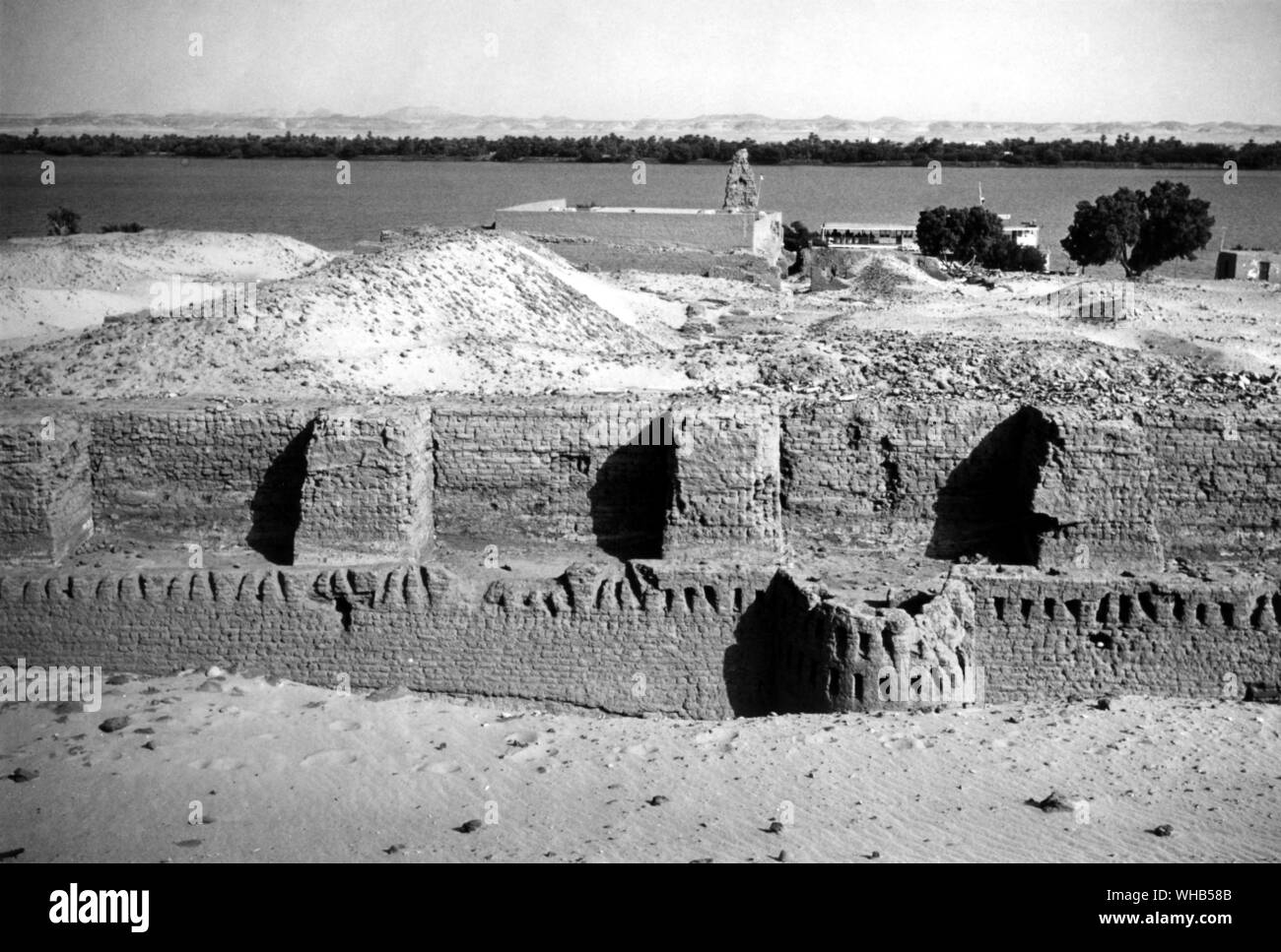 Mud brick walls of the fort at Buhen with temple of Hatshepsut in view. Buhen was an ancient Egyptian settlement situated below the Second Cataract. The fortress was probably constructed during the rule of Senusret III, around 1860 BC (12th dynasty). It was submerged by Lake Nasser created by the Aswan Dam in 1964.. . . Stock Photo