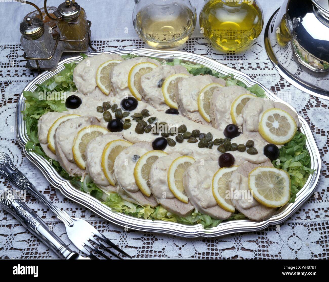 Food well presented on a silver platter - meat, lemon slices, capers, olives, sauce and shredded lettuce - possibly pork loin or ham?. Stock Photo