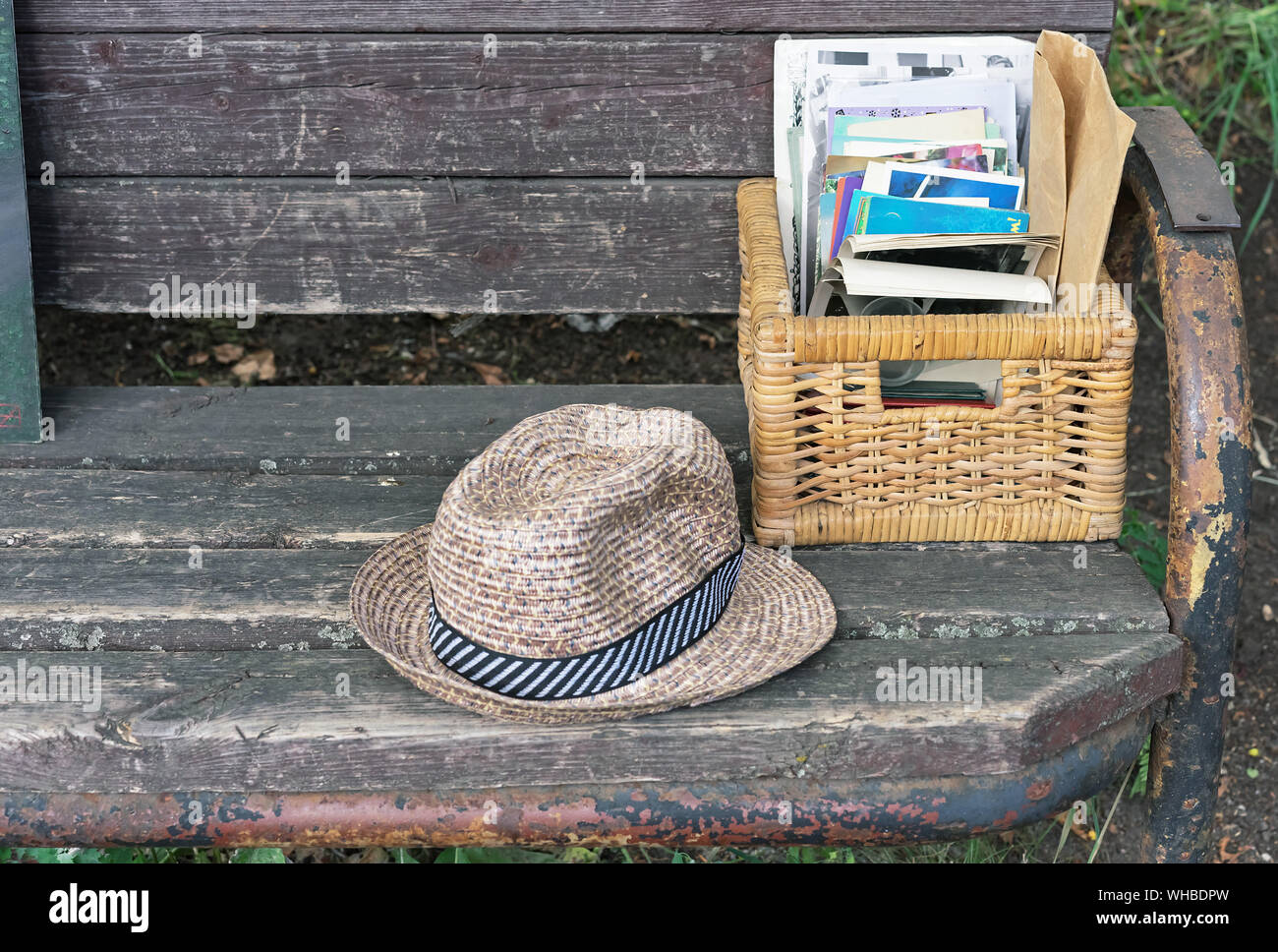 Vintage straw hat and a wicker basket with photos lie on a park bench ...