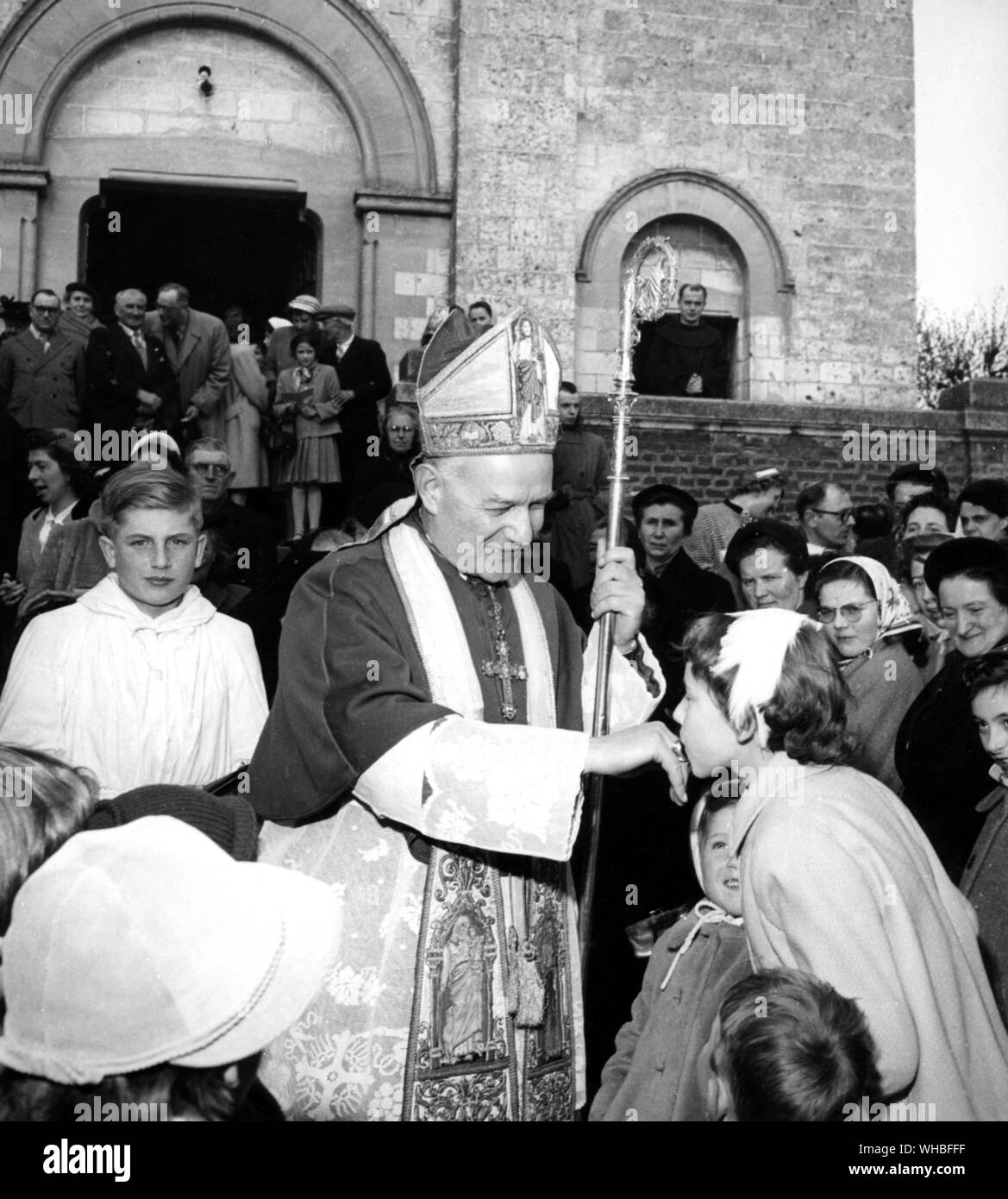Roman Catholic bishop having his ring kissed by a young girl surrounded by a crowd of people outside church Stock Photo