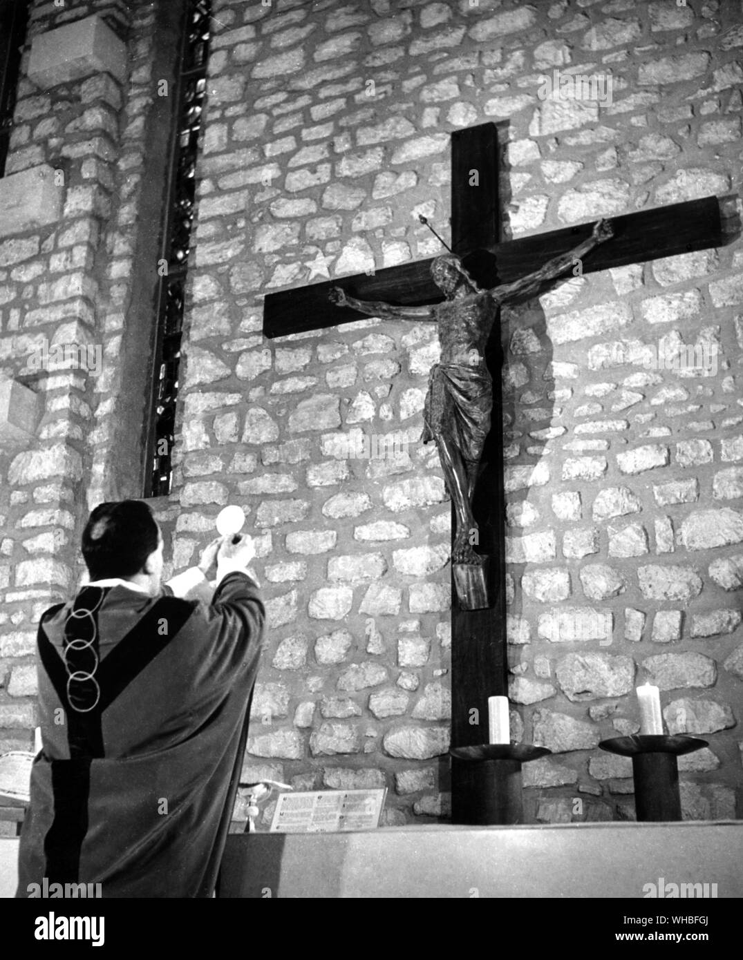 Taking the host in his hands, the celebrant speaks over it, and overall the other hosts, the word of consecration. Then he raises it for all to see. A bell is rung and the people bow their in adoration Stock Photo