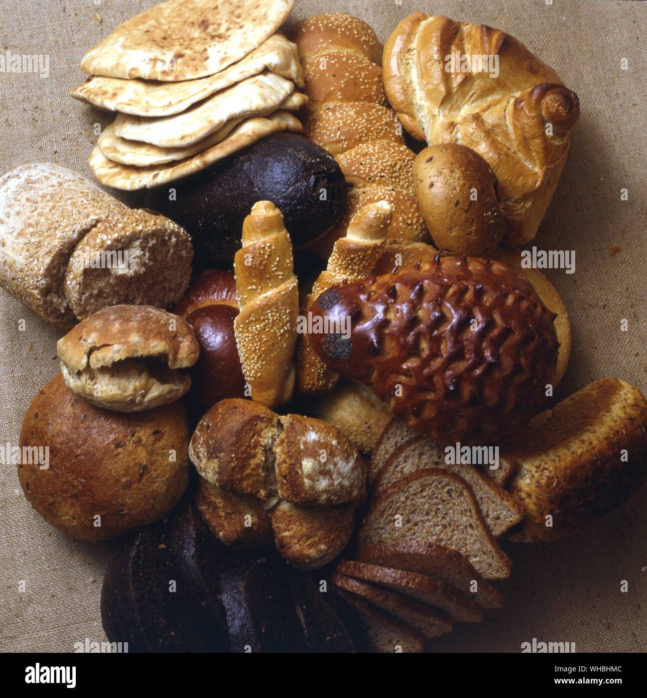 A display of different types of bread including pitta , wholemeal , sliced loaf , roll , sesame seed , knotted . Stock Photo