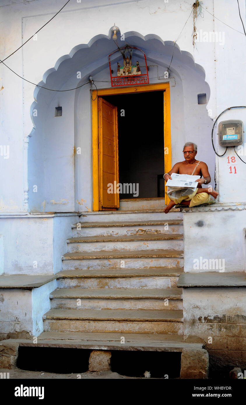 A man sits reading newspaper at the entrance of his house in Pushkar twon in Rajasthan India. Pushkar is one of the oldest towns in India and is a fav Stock Photo
