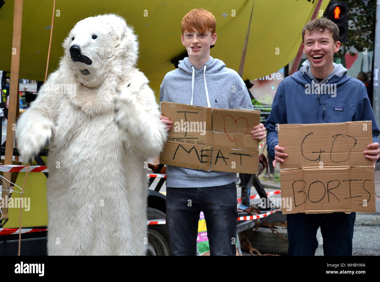 A person in a polar bear suit on Deansgate with young men holding ironic messages: 'I Love Meat' and 'Go Boris'. Northern Rebellion protesters, part of the global movement Extinction Rebellion, marched through Manchester, uk, and held a series of die-ins to urge for action on climate change on September 2nd, 2019. Protest sites included Barclays Bank, a Primark store and HSBC Bank. This was the fourth day of a protest which blocked Deansgate, a main road in central Manchester. Stock Photo