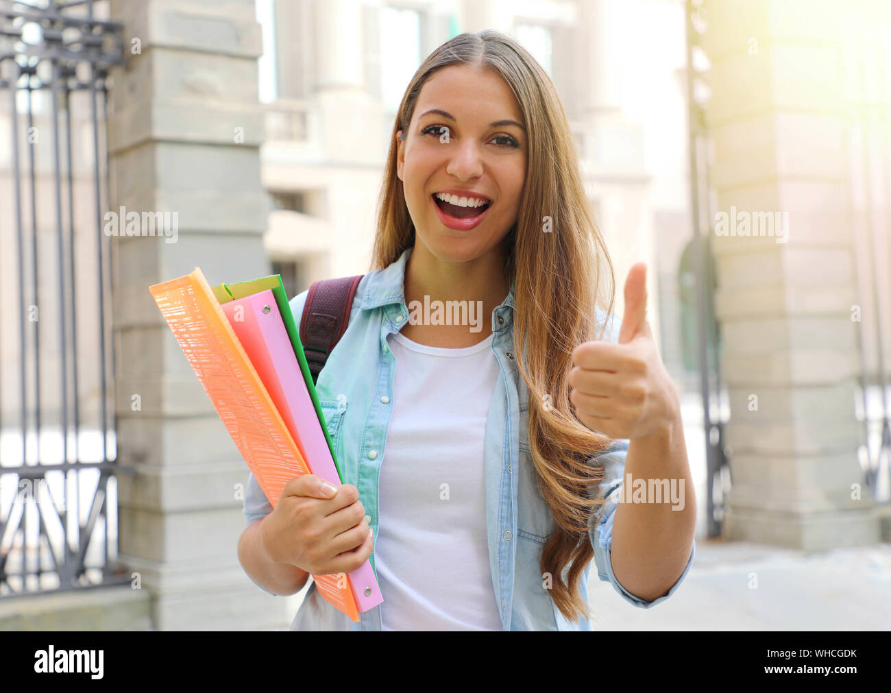 Happy student girl doing student exchange programme in Europe. Young woman gives thumb up outdoor. Stock Photo